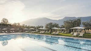 Une piscine entourée d’arbres et de montagnes, avec des chaises longues et des parasols.