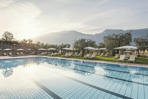 A swimming pool with lounge chairs and umbrellas, surrounded by trees and mountains. - "Villa Imelda" spacious, bright apartments, garden or balcony, lake view (Limone Sul Garda)
