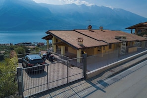 Un immeuble résidentiel avec un toit recouvert de tuiles, une allée bordée d’une clôture et une vue sur un lac et des montagnes en arrière-plan.