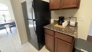 A kitchen with a black refrigerator, wooden cabinets, a granite countertop, a coffee maker, and a sign that reads "Fresh Brewed Coffee". - Modern Cozy 3BR Home in Forney (Forney)