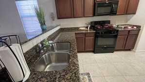 A kitchen with granite countertops, stainless steel sinks, wooden cabinets, a microwave, an oven, and a window with a view. - Modern Cozy 3BR Home in Forney (Forney)