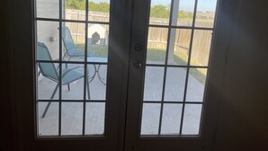 A view through a door with a grid pattern, leading to an outdoor patio with a wooden fence, a metal table, and two green chairs. - Modern Cozy 3BR Home in Forney (Forney)
