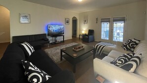 A living room with a flat-screen TV, black and white sofas, a coffee table, and a window with a view. - Modern Cozy 3BR Home in Forney (Forney)