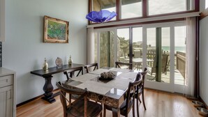 A dining area with a table set for four, a painting on the wall, and a view of the ocean through large windows.