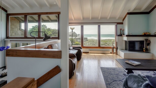 A modern living room with a large window overlooking the sea, a fireplace, and a cozy seating area.