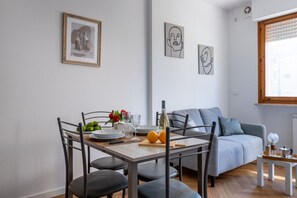 Zona pranzo con tavolo imbandito per quattro persone, divano e opere d'arte alle pareti.