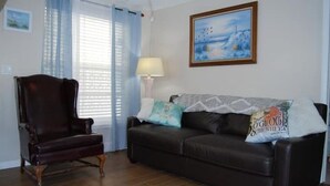 Un salon avec un canapé en cuir marron foncé, un fauteuil assorti et un tableau accroché au mur.