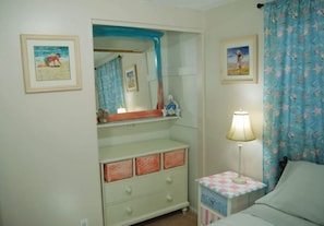 Et soveværelse med en seng, et natbord med lampe, en kommode med skuffer, et spejl og to billeder hængende på væggen.