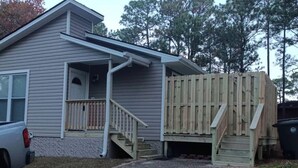 A single-story house with a front porch, a wooden deck, and a gravel driveway. - Perfect Fayetteville Stay-cation in Cozy 2-Bed, 2-Bath Townhome (Fayetteville)