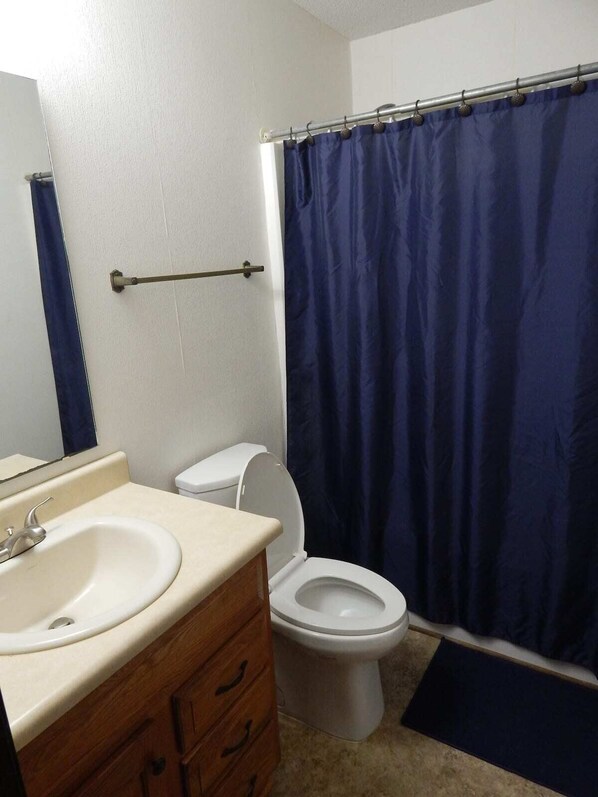A bathroom with a white sink, wooden vanity, a white toilet, and a blue shower curtain. - Perfect Fayetteville Stay-cation in Cozy 2-Bed, 2-Bath Townhome (Fayetteville)