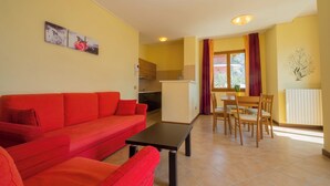 A living room with a red sofa, a dining table with chairs, and a kitchen area in the background. - "Villa Imelda" spacious, bright apartments, patio or balcony, lake view (Limone sul Garda)