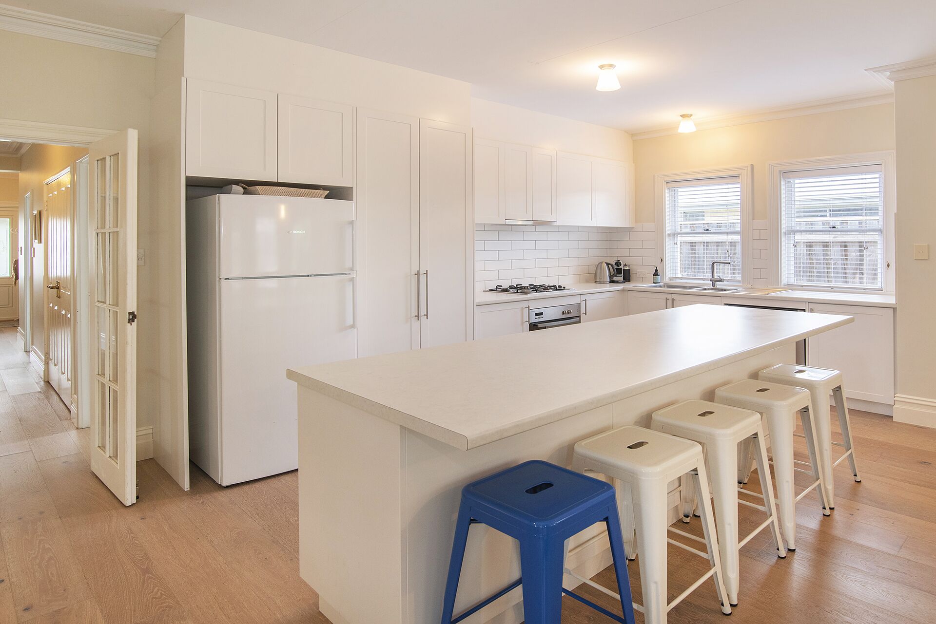 A modern kitchen with white cabinetry, a central island with bar stools, and a refrigerator.