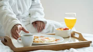 A tray with a cup of coffee, toast, a glass of orange juice, and a bowl of fruit on a bed.