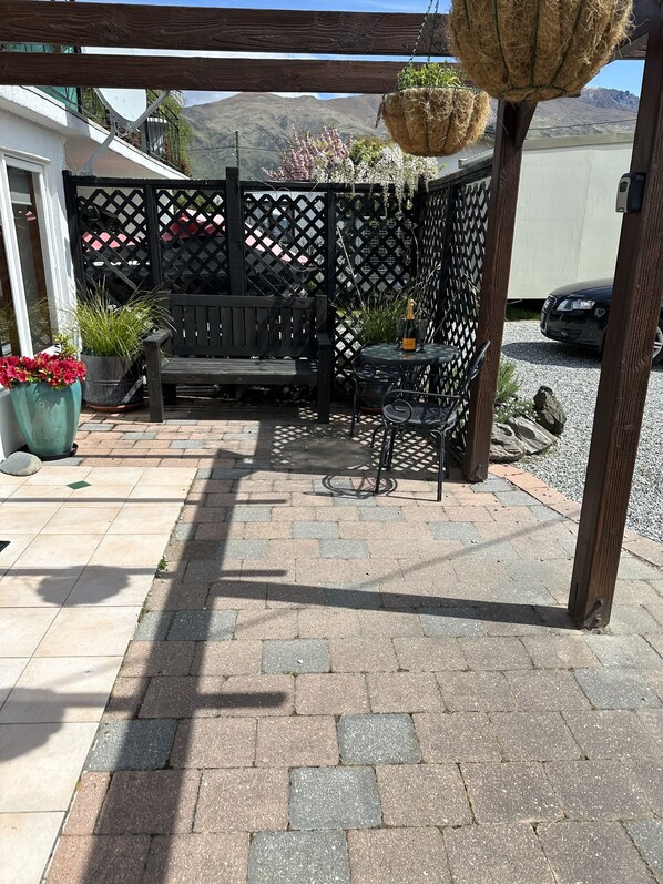 A patio with a wooden bench, a table with chairs, and hanging planters.