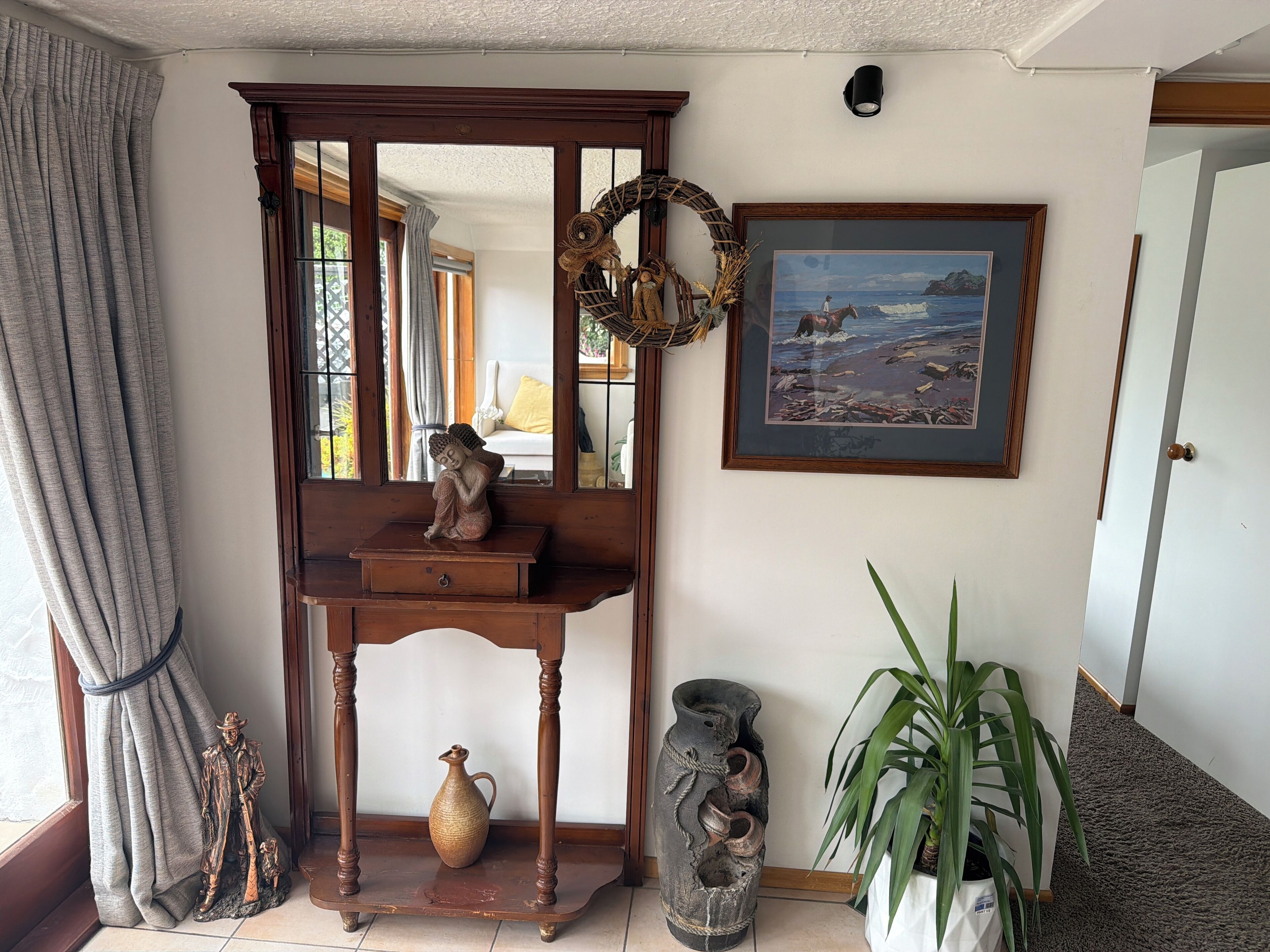 A room with a wooden console table, a statue, a vase, a framed painting, and a potted plant.