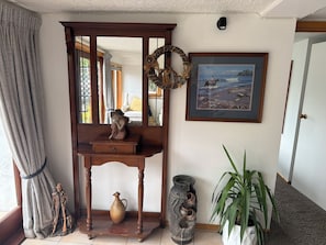 A room with a wooden console table, a statue, a vase, a framed painting, and a potted plant.