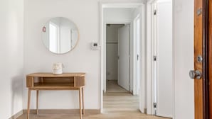 A hallway with a wooden table and a round mirror on the wall. - JOIVY Striking flat in Benfica (Lisboa)