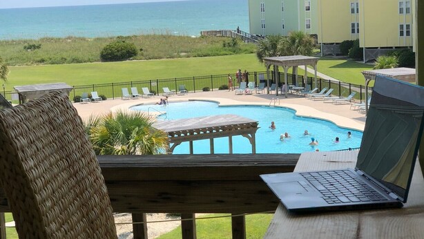 A view of a pool area with lounge chairs and a laptop on a table. - OceanScape- Beach and Sun in Surf City! (Surf City)