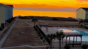 A residential area with a swimming pool, a covered patio, and a view of the sunset over the water. - OceanScape- Beach and Sun in Surf City! (Surf City)