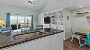 A modern kitchen with white cabinets, a granite countertop, and a built-in TV. - OceanScape- Beach and Sun in Surf City! (Surf City)