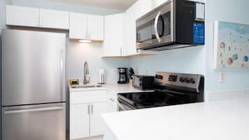 A modern kitchen with white cabinets, a stainless steel refrigerator, a microwave, a toaster, and a stove.