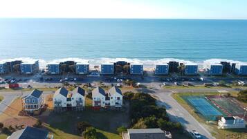 A coastal residential area with multiple blue buildings, a parking lot, and a tennis court.