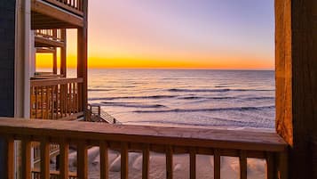 A wooden balcony overlooking a beach with a sunset view.