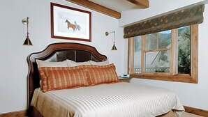A bedroom with a wooden bed, a framed picture on the wall, and a window with a view of trees. - Innsbruck Aspen | Deluxe One-Bedroom Junior Suite 03 w/ Hot tub, Centrally located (Aspen)