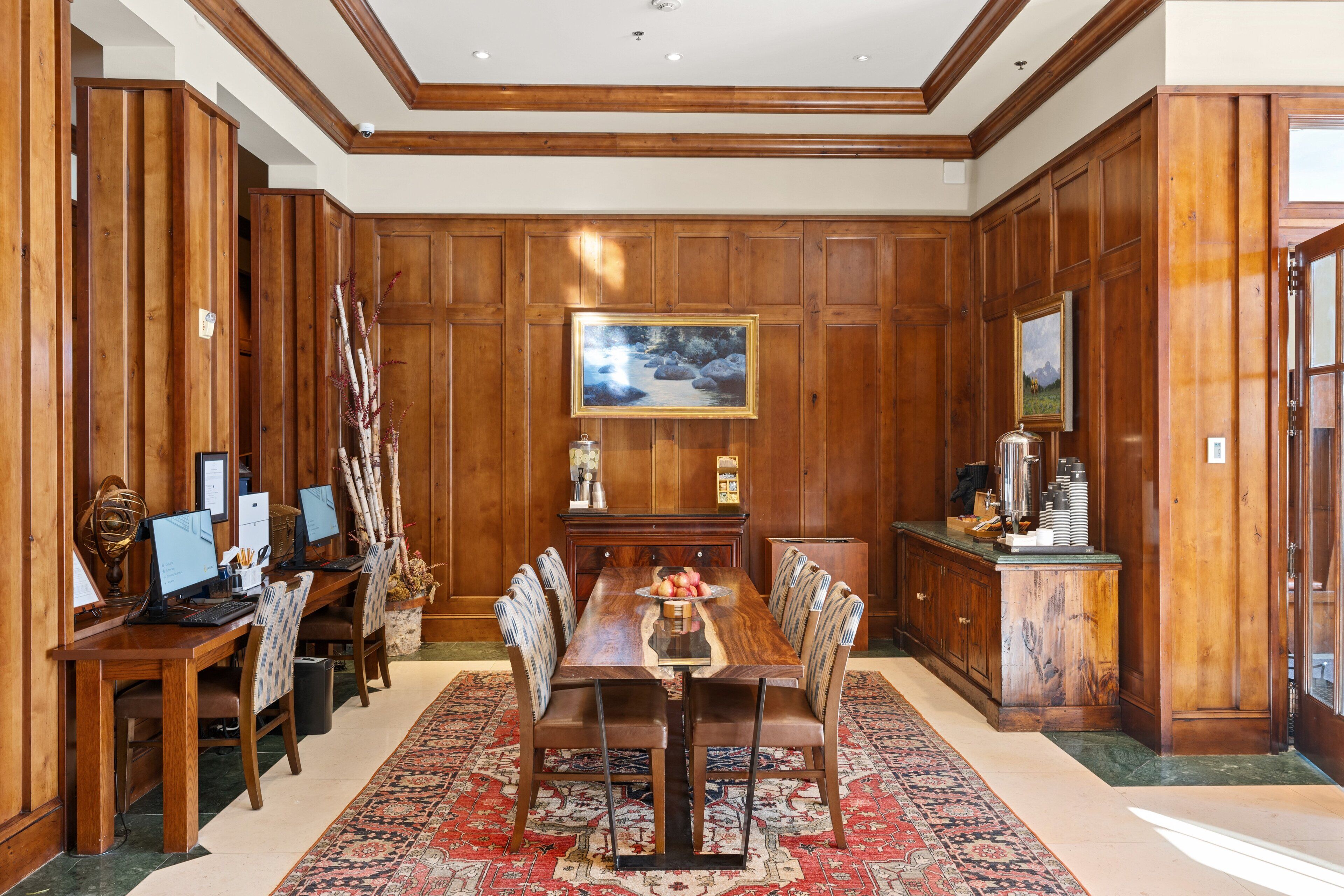 A formal dining room with a long wooden table, six chairs, and a red patterned rug.