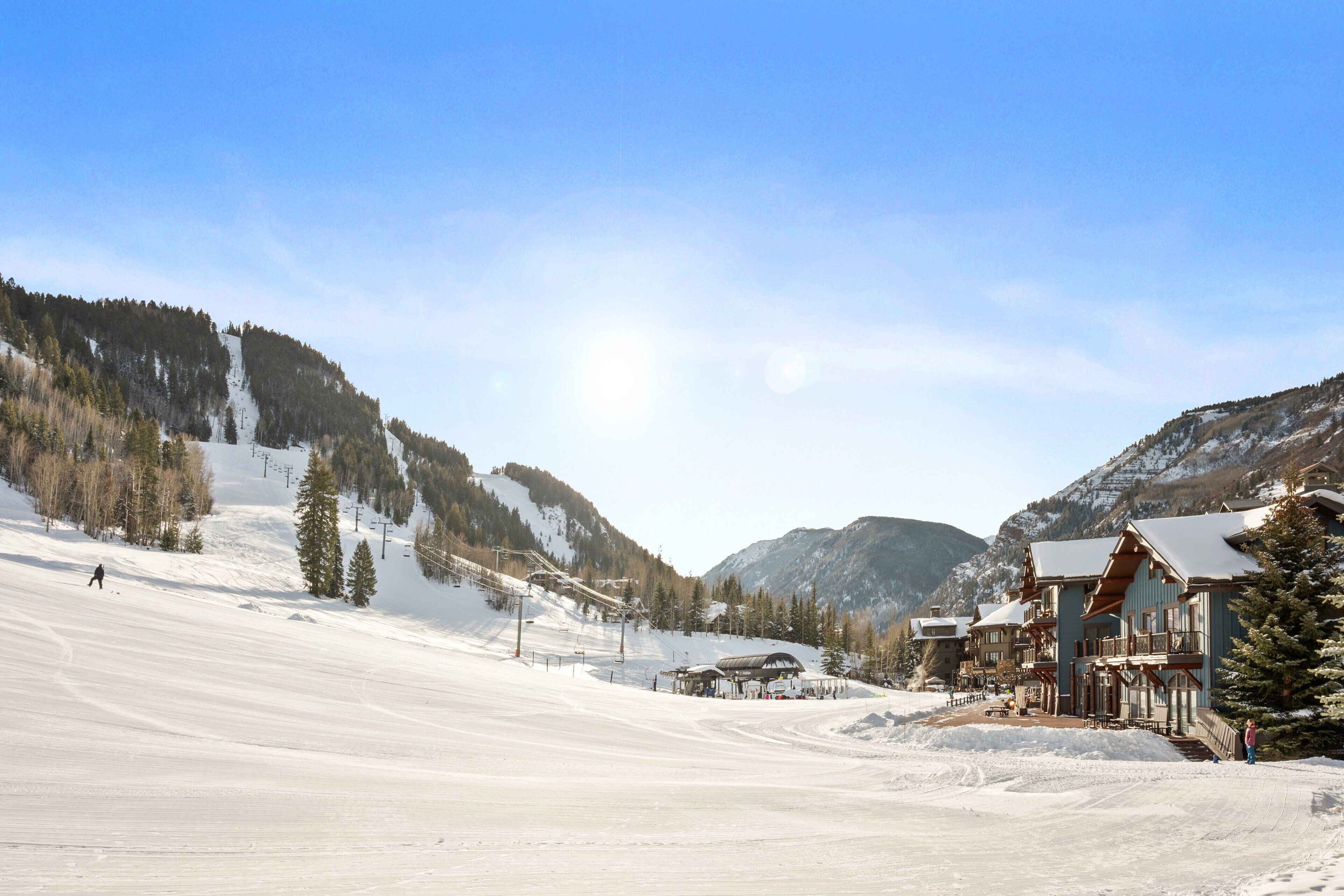 A snow-covered ski slope with a lodge featuring a wooden exterior and a ski lift in the background.