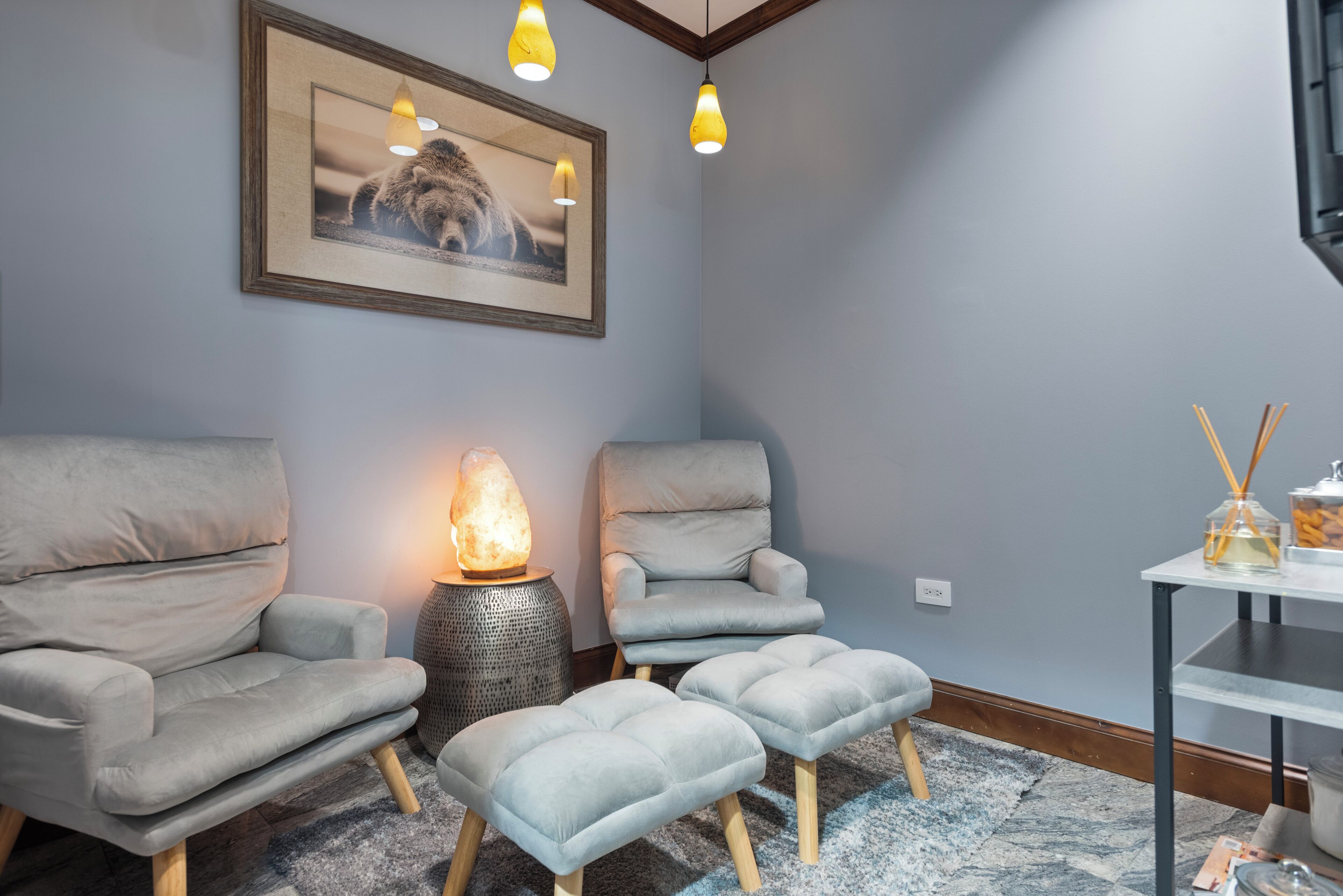 Een moderne kamer met twee grijze fauteuils, een bijzettafeltje met een diffuser en een verwarmde steen.