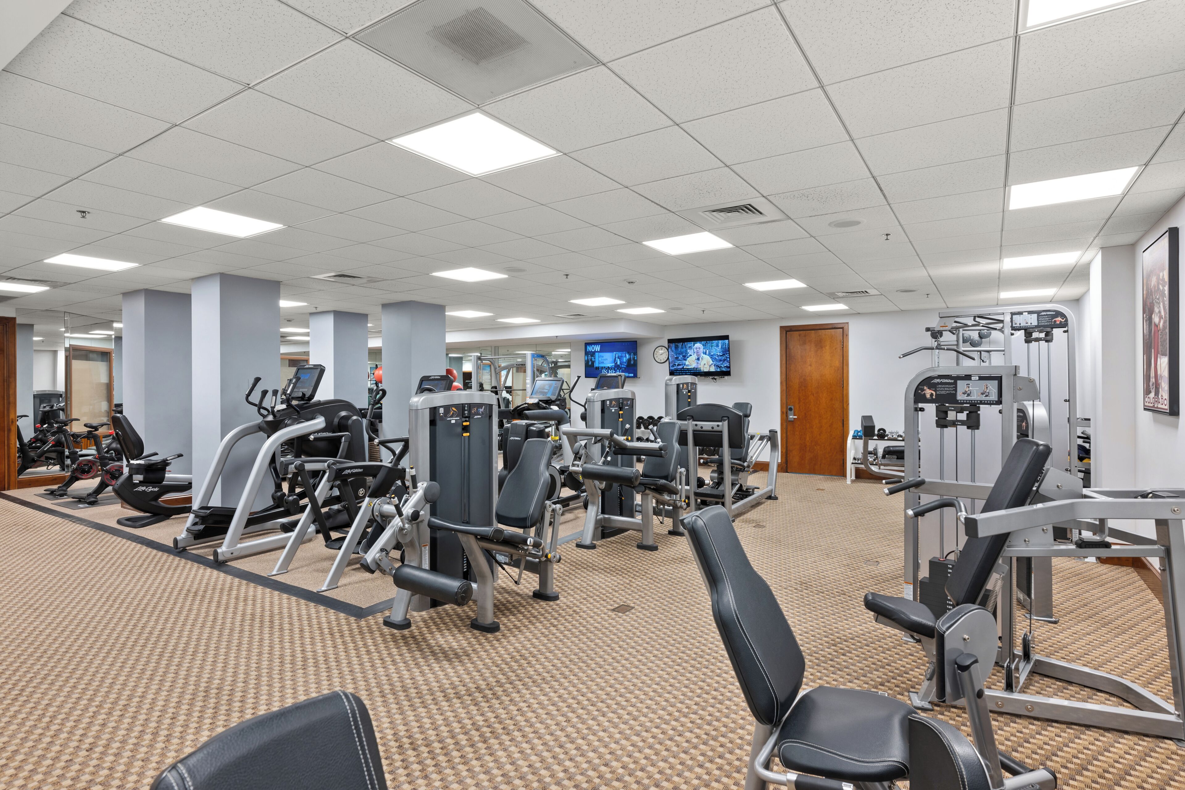 A gym with various exercise machines, a television, and a carpeted floor.