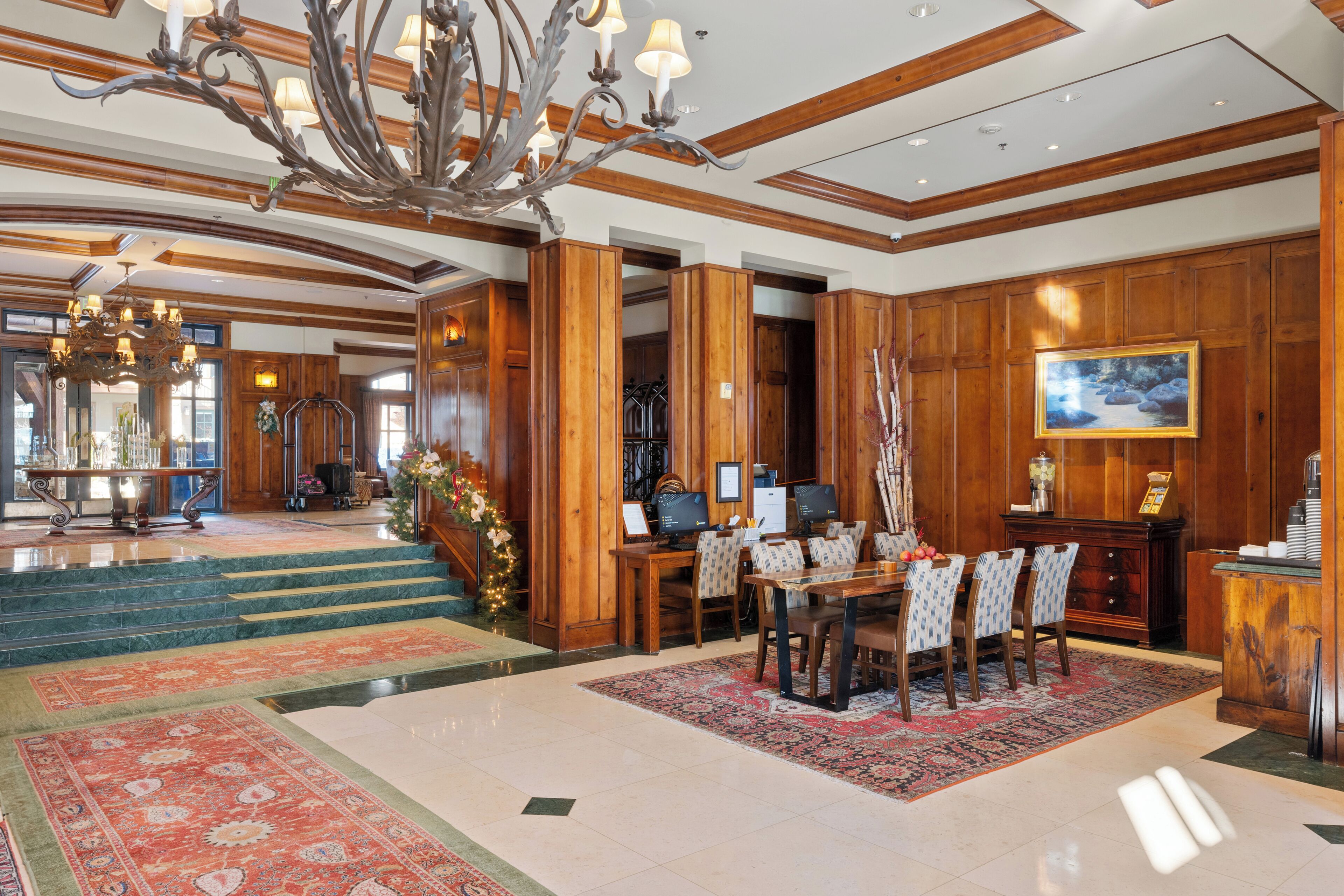 A spacious lobby with a grand chandelier, wooden paneling, and a dining area with a large table and chairs.