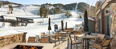 An outdoor patio with stone seating and a fire pit, overlooking a snowy mountain area with a ski lift and a building labeled "Hotel Centro."