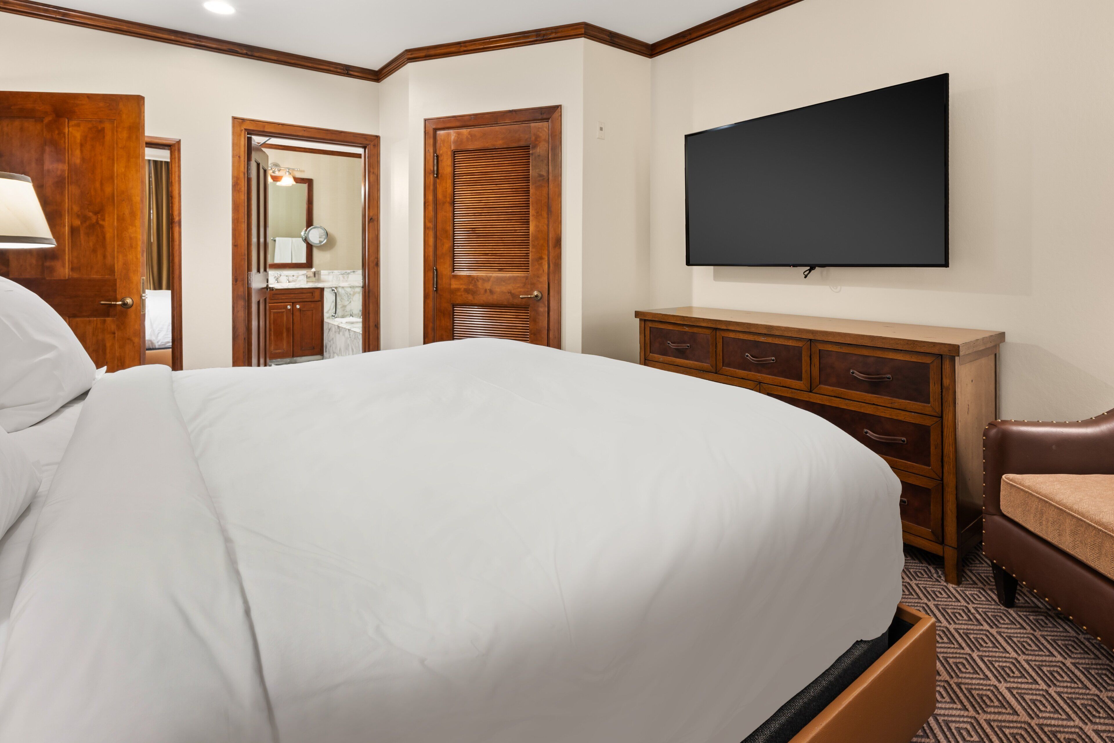 Une chambre d’hôtel avec un grand lit, une armoire en bois, un téléviseur fixé au mur et une salle de bain visible à travers une porte ouverte.