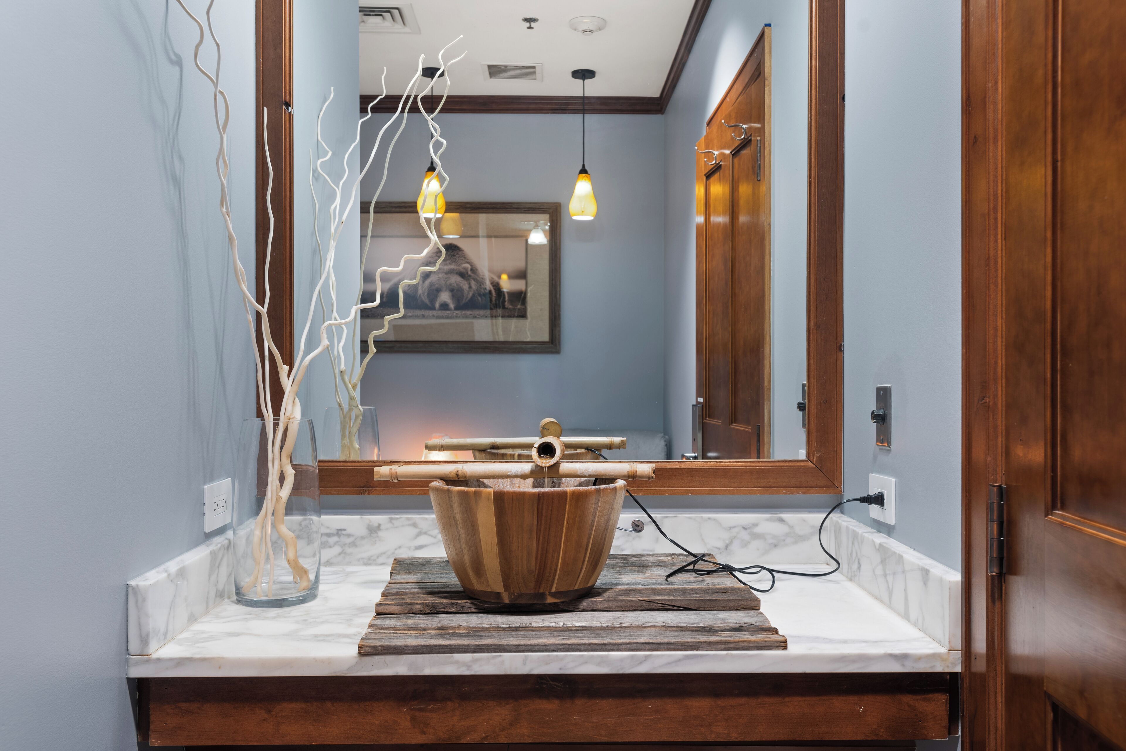 Une salle de bain avec un lavabo en forme de bol en bois, un comptoir en marbre et un miroir qui reflète un escalier.