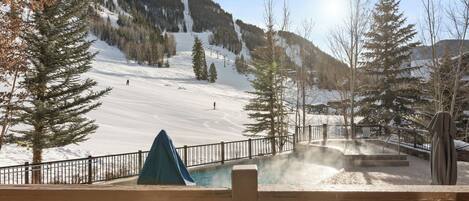A ski resort with a chairlift, a hot tub area, and a snowy mountain backdrop.