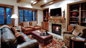 Ein gemütliches Wohnzimmer mit Ledersofas, einem Kamin, einem Fernseher und einem Bücherregal.