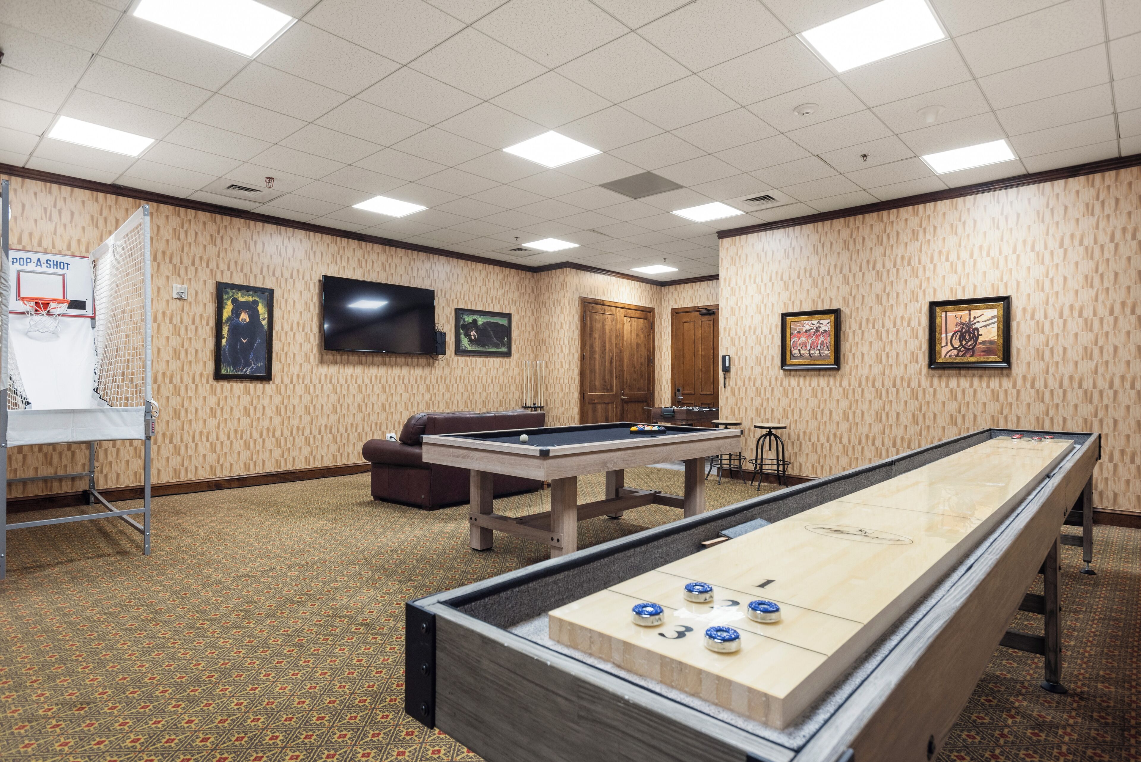 Una habitación con mesa de billar, mesa de fútbol de mesa, mesa de billard y televisor montado en la pared, además de una puerta.