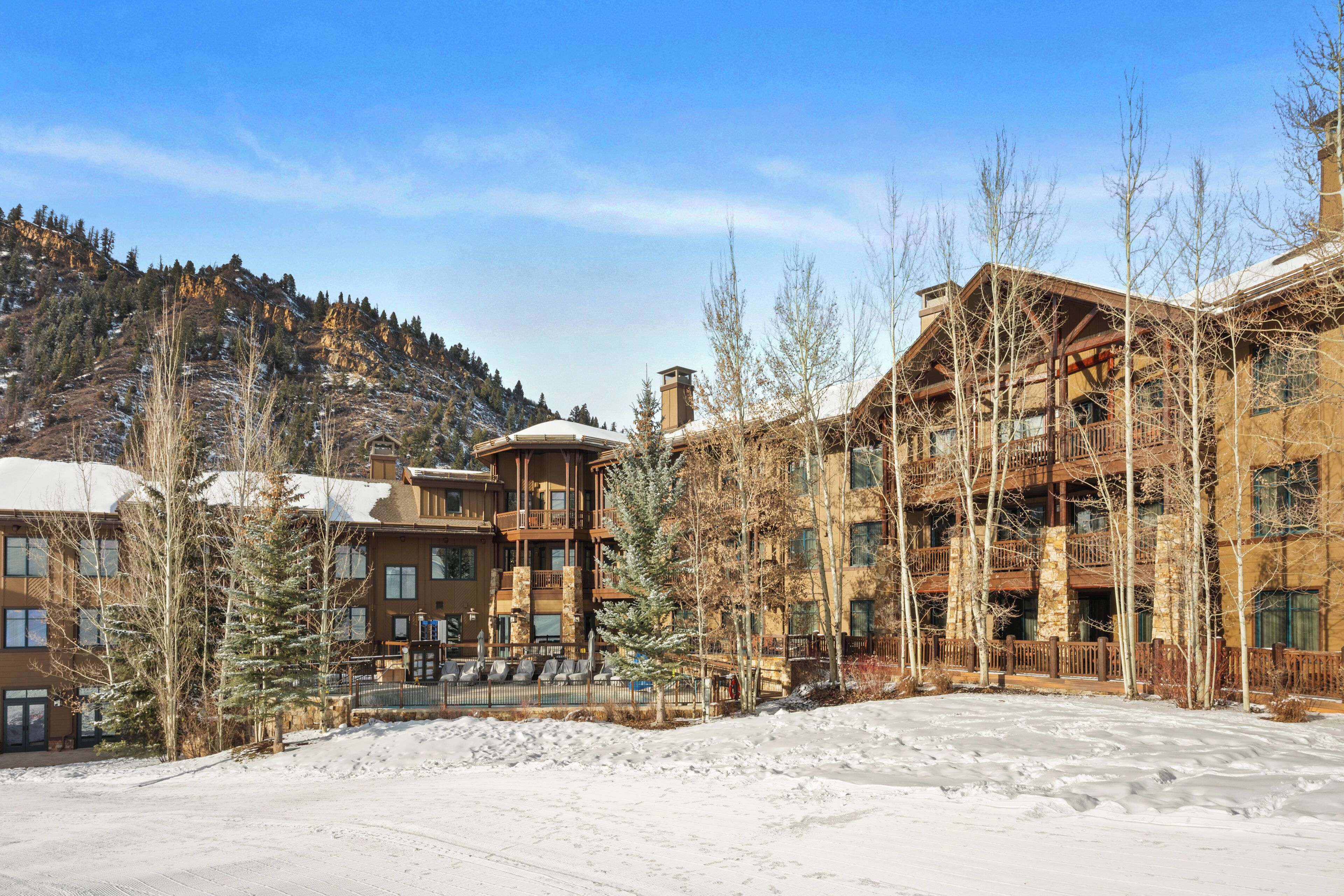 Un chalet à plusieurs étages, avec une piste de ski au premier plan, entouré d’arbres et de montagnes couverts de neige.
