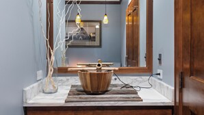 Une salle de bain avec un lavabo en forme de bol en bois, un comptoir en marbre et un miroir qui reflète un escalier.
