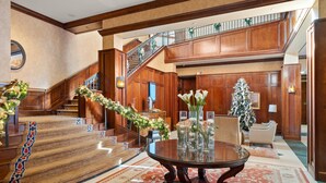 Um amplo hall com uma escadaria, uma mesa redonda com vasos e um pinheiro de Natal.