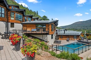 Un moderno edificio a più piani con piscina, area salotto esterna e montagne sullo sfondo.