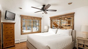 Een slaapkamer met een groot bed, een houten garderobe, een plafondventilator, een aan de muur bevestigde televisie en een raam met uitzicht.