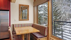 Eine gemütliche Küche mit Holztisch und Bank, einem Kühlschrank und einem großen Fenster mit Blick auf Bäume.