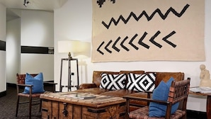 A modern living room with a brown leather sofa, blue cushions, a wooden coffee table, and a large wall art piece.