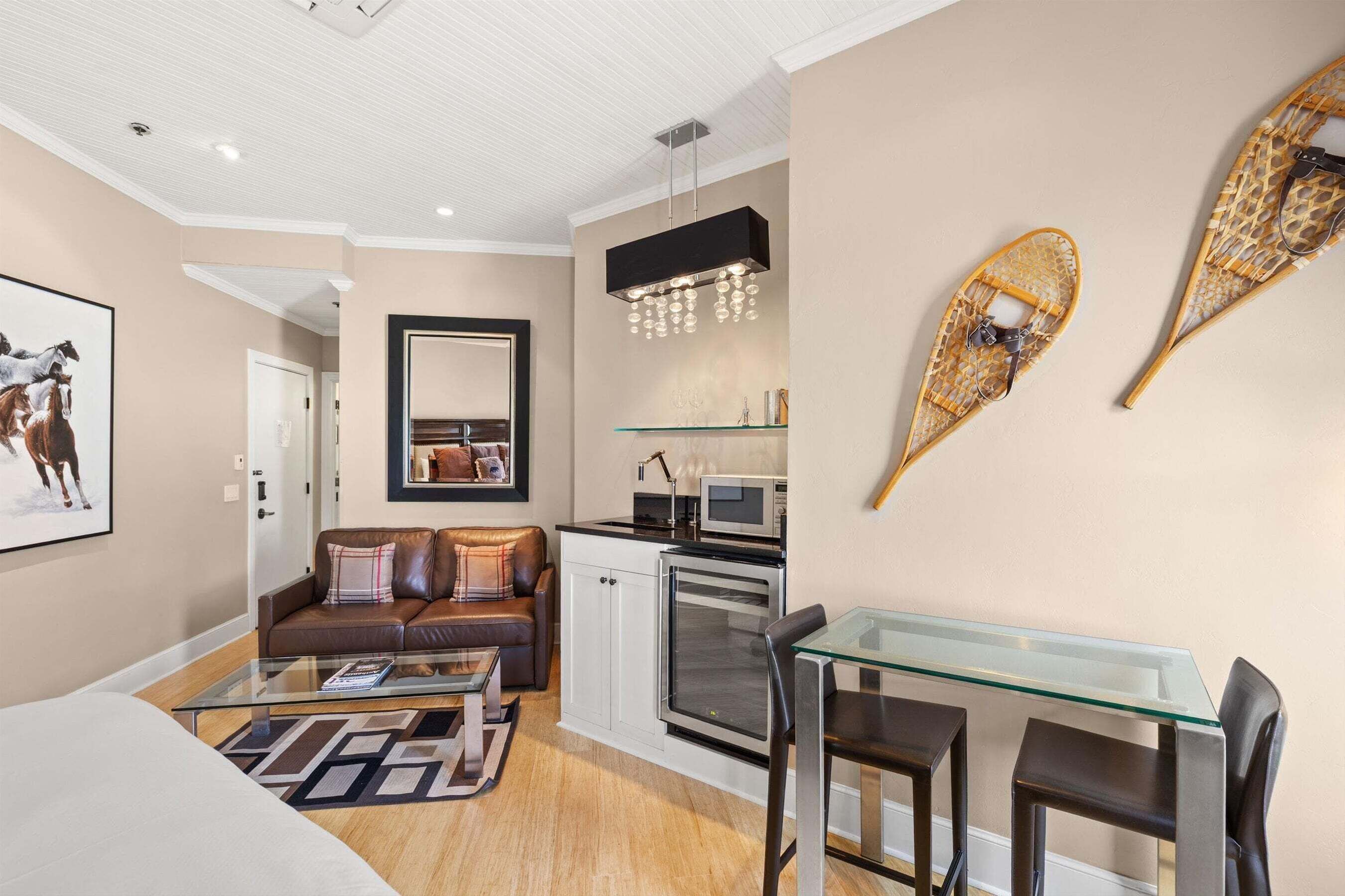Un espacio habitable compacto con kitchenette, zona de comedor y de estar con sofá y mesa de centro de vidrio.