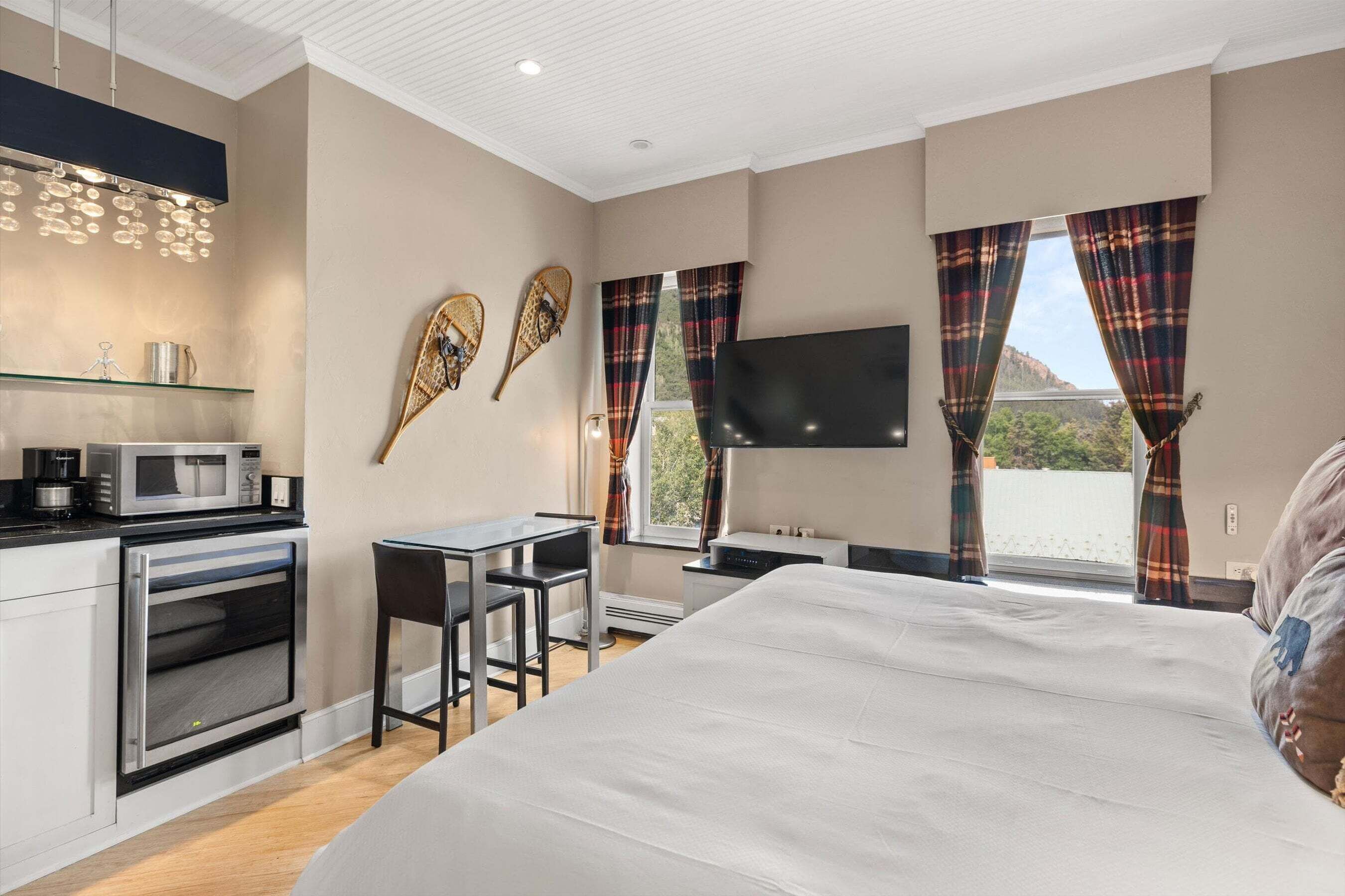 Quarto com cama, televisão, escrivaninha, cadeira, micro-ondas e pequena cozinha.