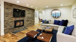 A modern living room with a stone wall, a fireplace, a large TV, a sofa, and a coffee table.
