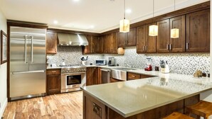A modern kitchen with wooden cabinets, stainless steel appliances, a large island, and pendant lighting.